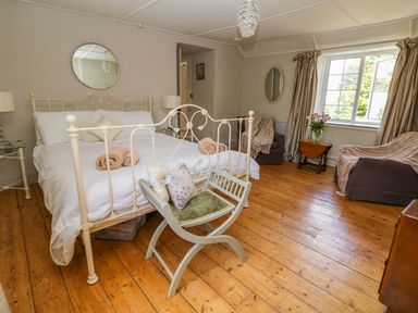 A bedroom with a white metal bed frame two rolled towels a wooden floor a green cushioned chair and two brown armchairs with a small wooden table under a window at Parwin in Tintagel