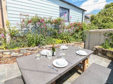 An outdoor dining area with a table set with plates glasses and a bottle in a garden at Parwin in Tintagel