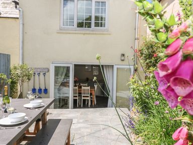 An outdoor patio with a table set for dining and garden tools hanging on the wall at Parwin in Tintagel