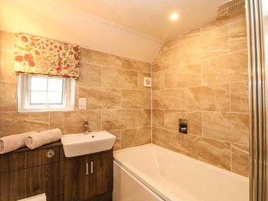 A bathroom with a bathtub sink wooden cabinet and a small window with floral blind at Parwin in Tintagel