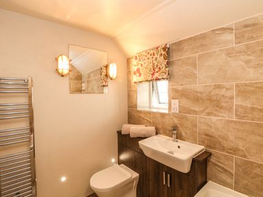 A bathroom with a toilet sink cabinet illuminated mirror window with floral curtain and towel rail at Parwin in Tintagel