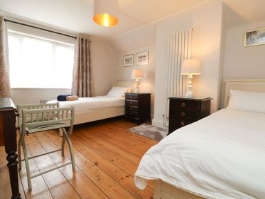 A bedroom with two single beds bedside tables lamps window and wooden floor at Parwin in Tintagel