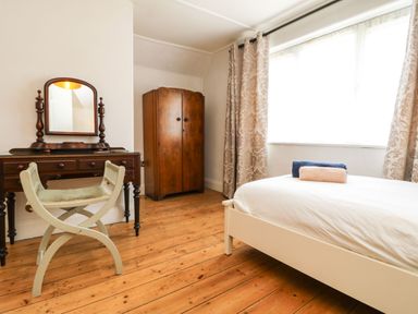A bedroom with a wooden floor a white bed with folded towels a wooden wardrobe a dressing table with a mirror and a chair at Parwin in Tintagel