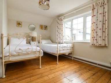 A bedroom with two single metal beds a small white nightstand with a lamp wooden floor and a large window with patterned curtains at Parwin Tintagel