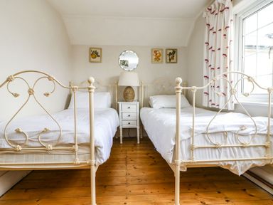 A bedroom with two single metal frame beds a bedside table with a lamp and framed pictures on the wall at Parwin in Tintagel