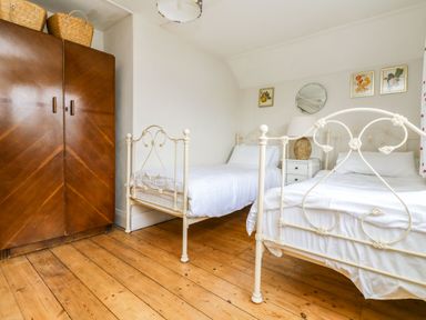 A bedroom with two white metal beds a wooden wardrobe a bedside table with a lamp and framed pictures on the wall at Parwin in Tintagel