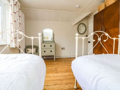 A bedroom with two white metal frame beds a green dresser with a mirror a wooden wardrobe and a chair near a window at Parwin in Tintagel