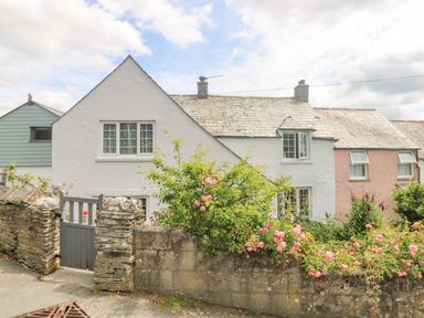 A stone and concrete wall with pink flowers and a gate in front of a semi detached house with white and pink walls at Parwin in Tintagel