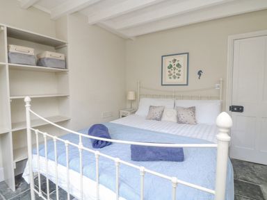 A bedroom with a metal framed bed and blue bedding beside a shelving unit with storage bins at Parwin Tintagel
