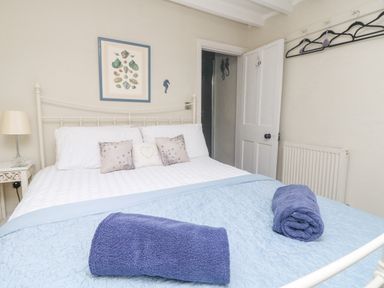 A bedroom with a white metal bed frame two purple towels on a light blue quilt and sea shell artwork above the bed at Parwin in Tintagel