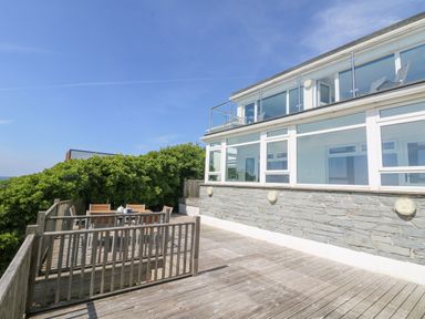 A balcony with wooden decking and outdoor dining set attached to a building with large windows at St Ives View in Porthtowan