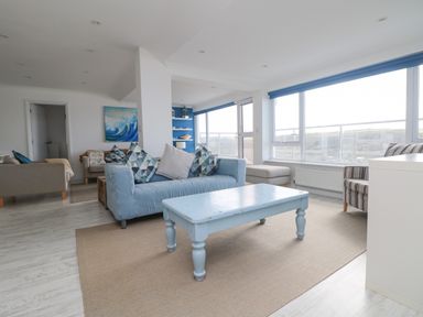 A living room with a blue sofa and table a striped armchair and large windows at St Ives View in Porthtowan