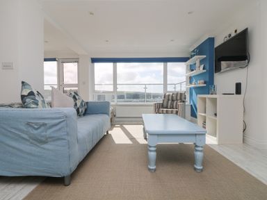 A living room with a blue sofa striped armchair blue coffee table wall-mounted tv and large windows at St Ives View in Porthtowan