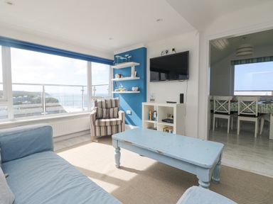 A living room with a blue sofa a striped armchair a blue coffee table a wall-mounted TV and a bookshelf at St Ives View in Porthtowan