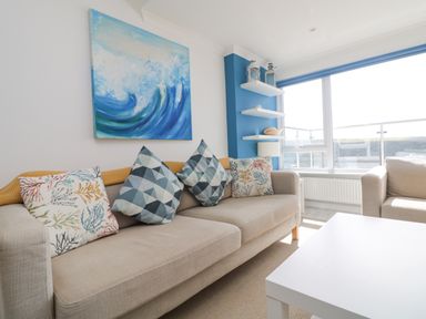 A living room with beige sofas and patterned cushions a white coffee table and a large window at St Ives View in Porthtowan