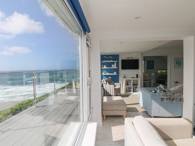 A living room with sofas a striped armchair a TV and shelves overlooking the ocean at St Ives View in Porthtowan