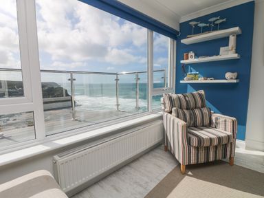A corner room with a striped armchair and three shelves on a blue wall overlooking the ocean at St Ives View in Porthtowan