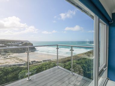 A balcony with glass railing overlooking a beach and ocean at St Ives View in Porthtowan