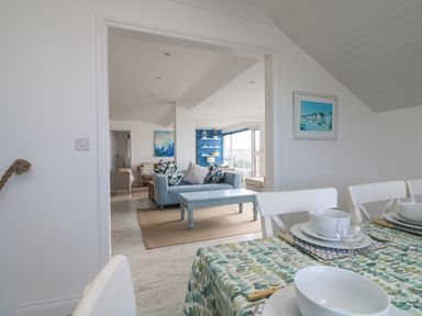 A dining area with a table set with bowls and glasses overlooking a living room with sofas and a coffee table at St Ives View in Porthtowan