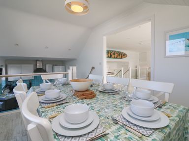 A dining table set with white plates, bowls, and glasses in a kitchen area at St Ives View in Porthtowan