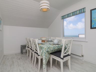 A dining room with a table set for six near a window with a sea view at St Ives View in Porthtowan