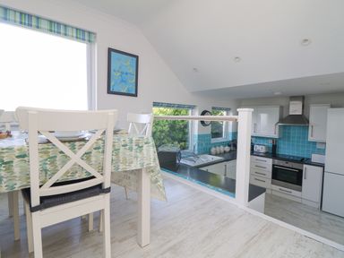 A dining table with chairs next to a kitchen with white cabinets and blue tiled backsplash at St Ives View in Porthtowan