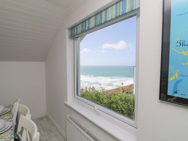 A dining area with white chairs and a table near a window showing an ocean view at St Ives View in Porthtowan