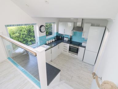 A kitchen with white cabinets blue tiled backsplash and appliances at St Ives View in Porthtowan