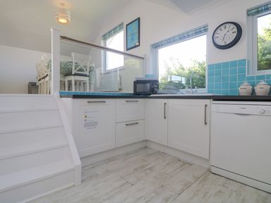 A kitchen with white cabinets blue tiled backsplash a microwave on the counter and a dining area with white chairs at St Ives View in Porthtowan