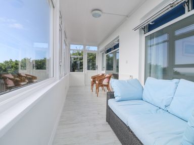 A sunroom with a wicker sofa with blue cushions and two wicker chairs with pink cushions at St Ives View in Porthtowan