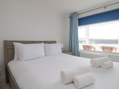 A bedroom with a bed made with white linens and towels on top near a window with blue curtains at St Ives View in Porthtowan