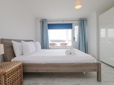 A bedroom with a wooden bed and white bedding blue curtains and a window with a view at St Ives View in Porthtowan