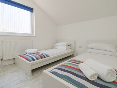 A bedroom with two single beds with striped blankets and rolled towels at St Ives View in Porthtowan