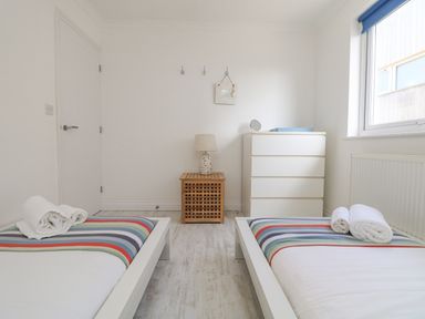 A bedroom with two single beds a wooden nightstand a lamp a chest of drawers and a window at St Ives View in Porthtowan