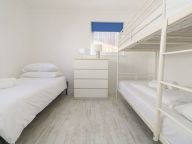 A bedroom with a single bed on the left bunk beds on the right and a chest of drawers under a window at St Ives View in Porthtowan
