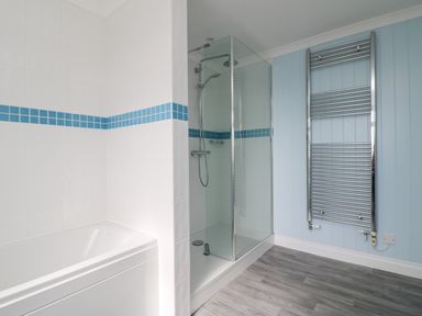 A bathroom with a bathtub, a glass-enclosed shower, a towel radiator, and wood flooring at St Ives View in Porthtowan