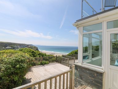 A wooden deck overlooking a beach and ocean with a glassed porch on the right at St Ives View in Porthtowan