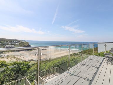 A balcony with glass railing overlooking a beach and ocean at St Ives View in Porthtowan
