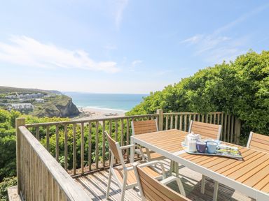 A wooden deck with a table and chairs overlooking the beach and ocean at St Ives View in Porthtowan