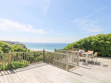 A wooden deck with a table and chairs overlooking the ocean and cliffs at St Ives View in Porthtowan