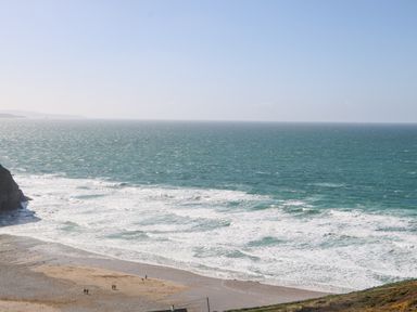 A beach with waves and a few people walking at St Ives View in Porthtowan