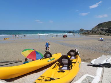 A sandy beach with yellow kayaks a colorful umbrella people walking and the sea in the background at St Ives View in Porthtowan
