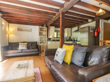 A living room with two leather sofas and cushions in front of a wooden coffee table open to a kitchen at Oaklands Near Boscastle