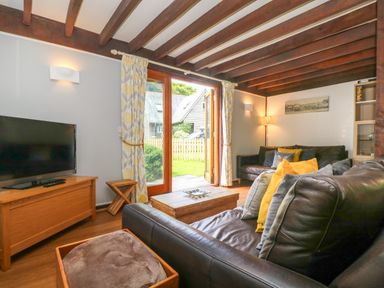 A living room with leather sofas and a wooden coffee table near glass doors leading to a garden at Oaklands Near Boscastle