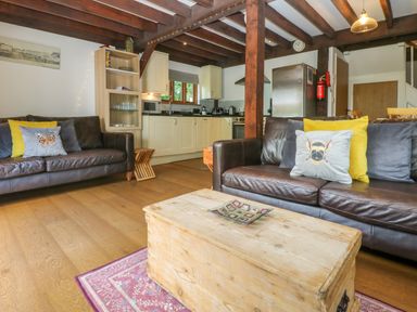 A living room with brown leather sofas and cushions next to a wooden chest coffee table and an open kitchen at Oaklands Near Boscastle