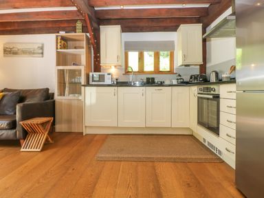 A kitchen with white cabinets wooden floor and a brown sofa near Oaklands Near Boscastle