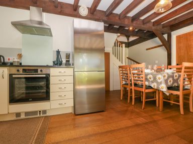 A kitchen with a stainless steel oven and fridge a dining table with chairs and a floral tablecloth under wooden ceiling beams at Oaklands Near Boscastle