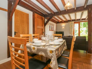 A dining room with a table set for six and wooden chairs next to a living area with sofas and a television at Oaklands Near Boscastle