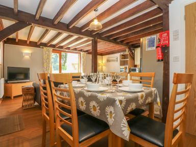 A dining area with a table set with bowls and glasses and wooden chairs in a room with exposed wooden beams at Oaklands Near Boscastle