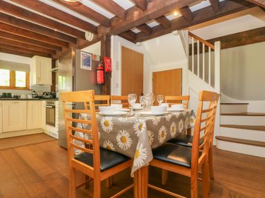 A dining table with chairs set for a meal near a kitchen and staircase at Oaklands Near Boscastle